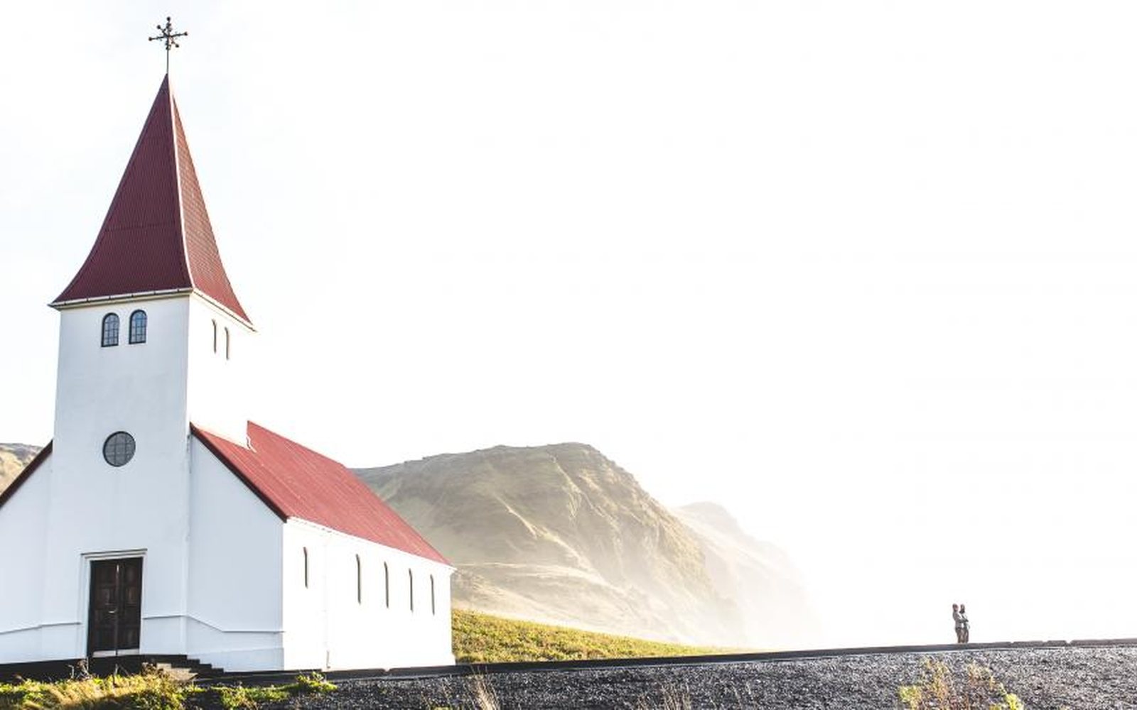 Small white church with a red roof in an open landscape.
